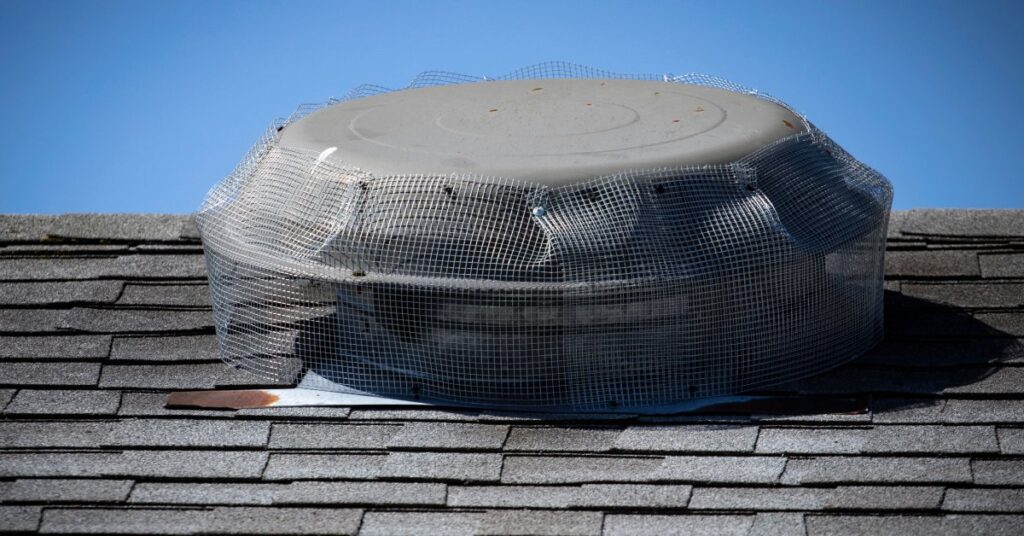 Wire mesh—used to prevent raccoon infestations in attics—installed tightly over a rooftop attic fan.