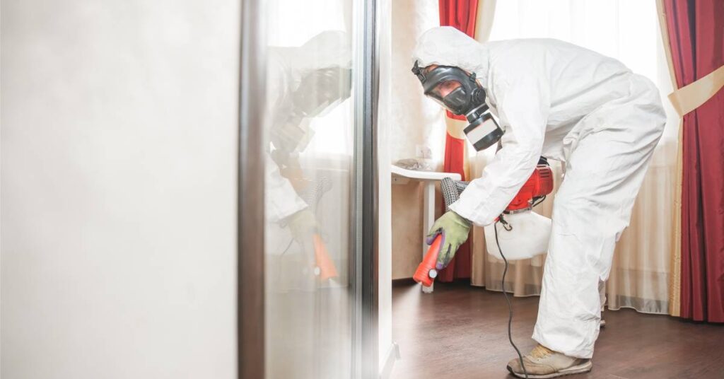 A professional rodent control specialist in a hazmat suit using a handheld rodent repellent spraying device.