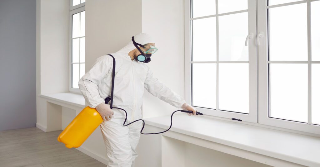 A rodent control specialist in protective gear and using a spraying device to exterminate and deter future infestations.