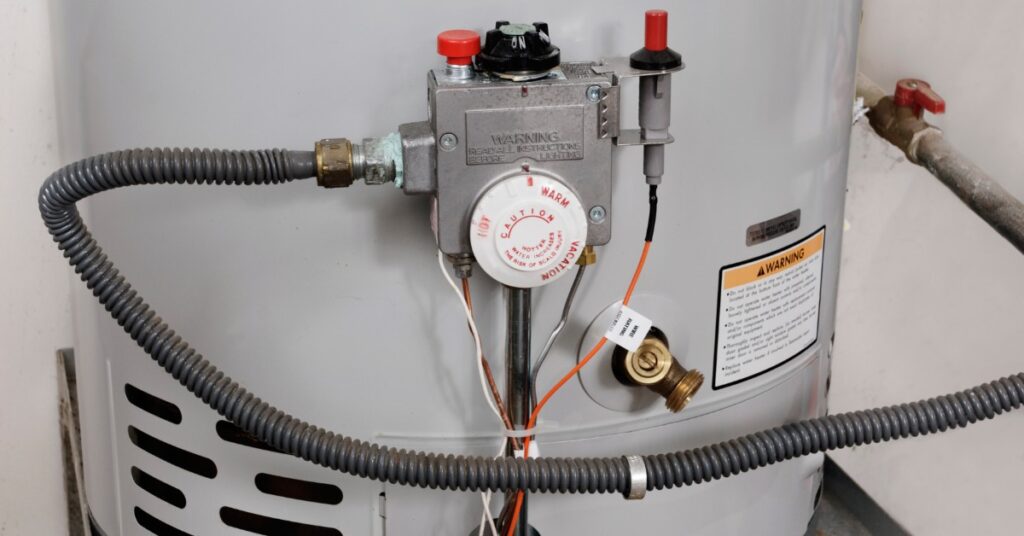 Close-up of a hot water heater, which features a dial set on "warm." It has a long gray tube traveling to a pipe.
